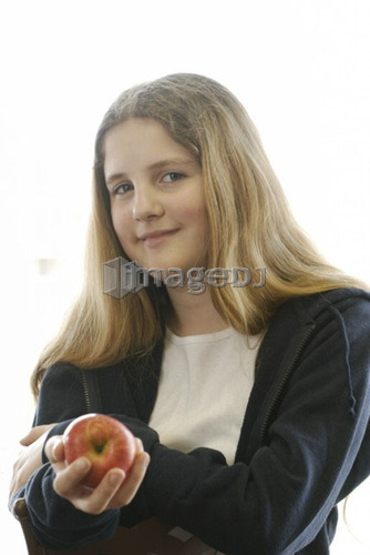 Pre-teen girl holding organic apple, wearing hoodie made with hemp fibre, Canada, Manitoba, Brandon