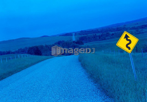 Blue toned winding rural road with bright yellow road sign, Canada, Alberta