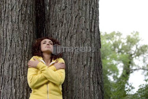 Woman with eyes closed leans against trunk of tree, Munson Park, Winnipeg, Canada