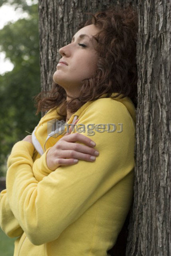 Side view of woman with eyes closed leans against trunk of tree, Munson Park, Winnipeg, Canada