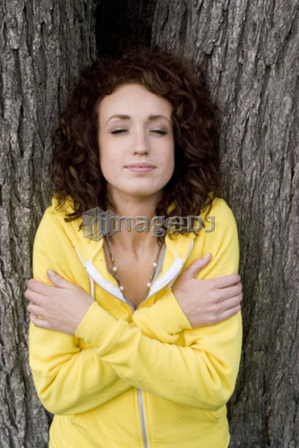 Woman with eyes closed leans against trunk of tree, Munson Park, Winnipeg, Canada