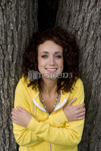 Smiling woman leans against large trunk of tree, Munson Park, Winnipeg, Canada