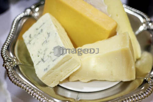 Bricks of blue, cheddar, parmesan, and brie cheese in a silver dish
