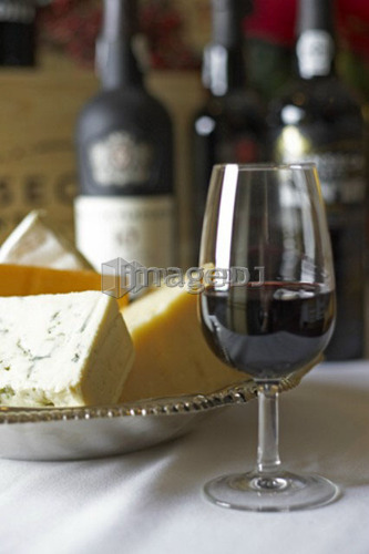 Glass of red wine with bricks of blue, cheddar, parmesan, and brie cheese in a silver dish