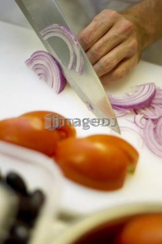 Detail of hand chopping red onion with sliced tomatoes in foreground
