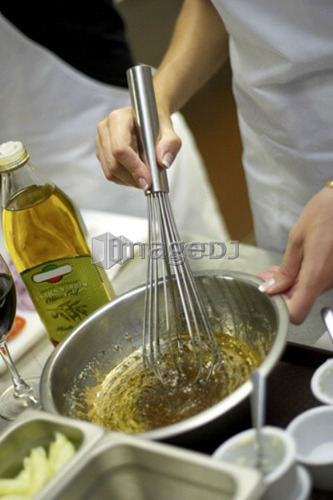 Person whisking bowl of olive oil with herbs and spices