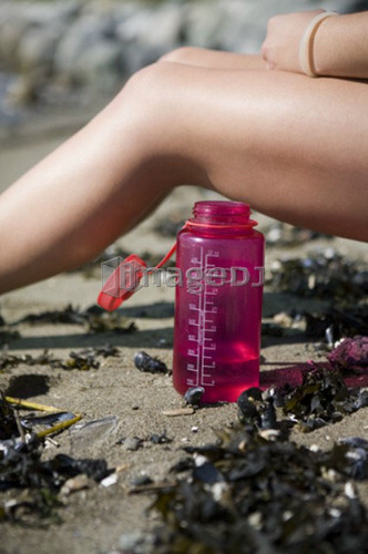 Crop image of female, 17, sitting at beach with water bottle, English Bay, Vancouver, BC