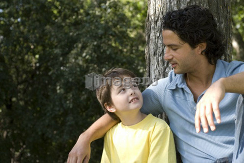Father with arm around six year old son beside large tree, Assiniboine Park, Winnipeg, Canada
