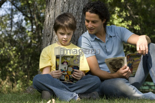 Father and son beside tree reading comic books, Assiniboine Park, Winnipeg, Canada