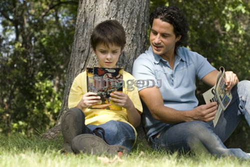 Father and son beside tree reading comic books, Assiniboine Park, Winnipeg, Canada