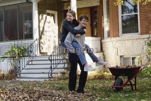 Teen brother and sister piggyback in autumn leaves, Winnipeg, Canada