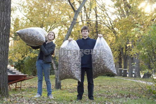 Teen brother and sister holding up bags of leaves for recycling, Winnipeg, Canada