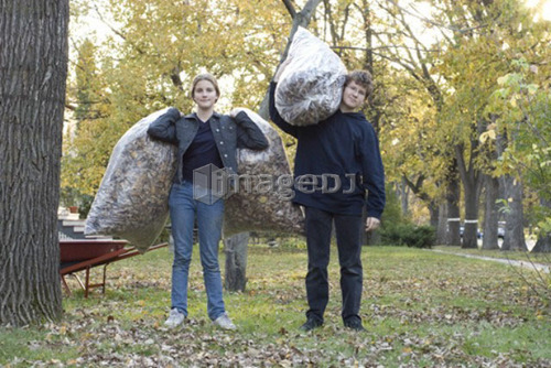 Teen brother and sister holding up bags of leaves for recycling, Winnipeg, Canada