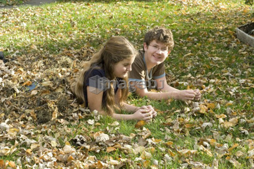 Teen brother and sister lying in leaves viewed from side, Winnipeg, Canada