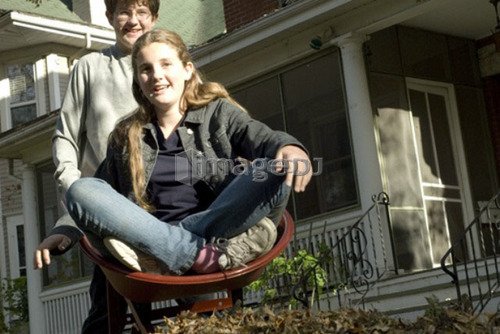 Teen brother carrying sister in wheelbarrow, Winnipeg, Canada